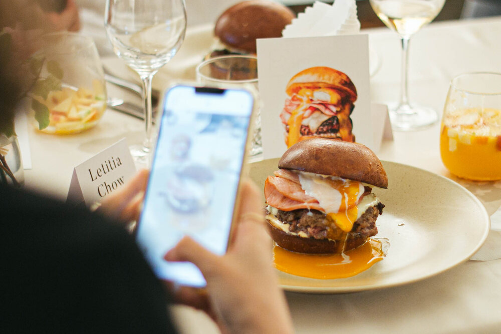 A plated dish beside a printed card illustrating the same dish, with a guest photographing it