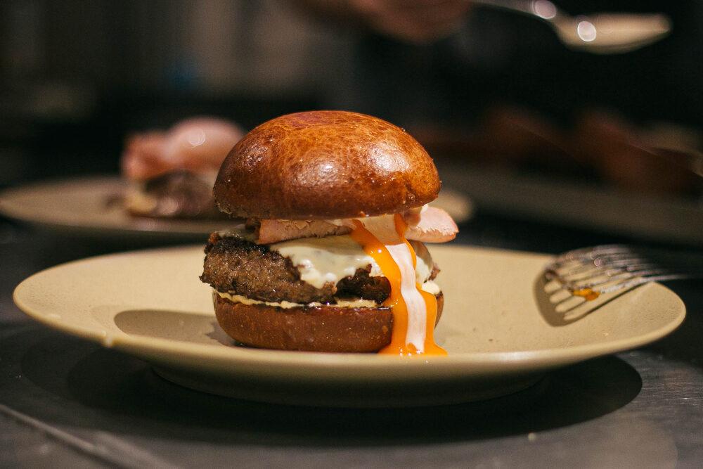 A plated burger beside a printed card illustrating the same dish, with a guest photographing it