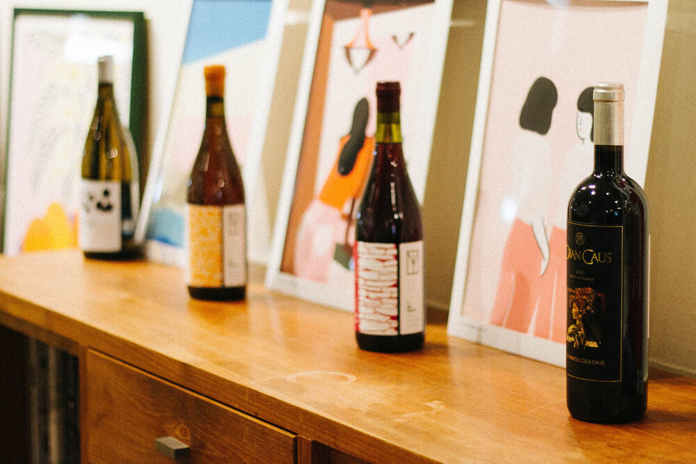Wine bottles lined up on a wooden counter in front of framed art prints