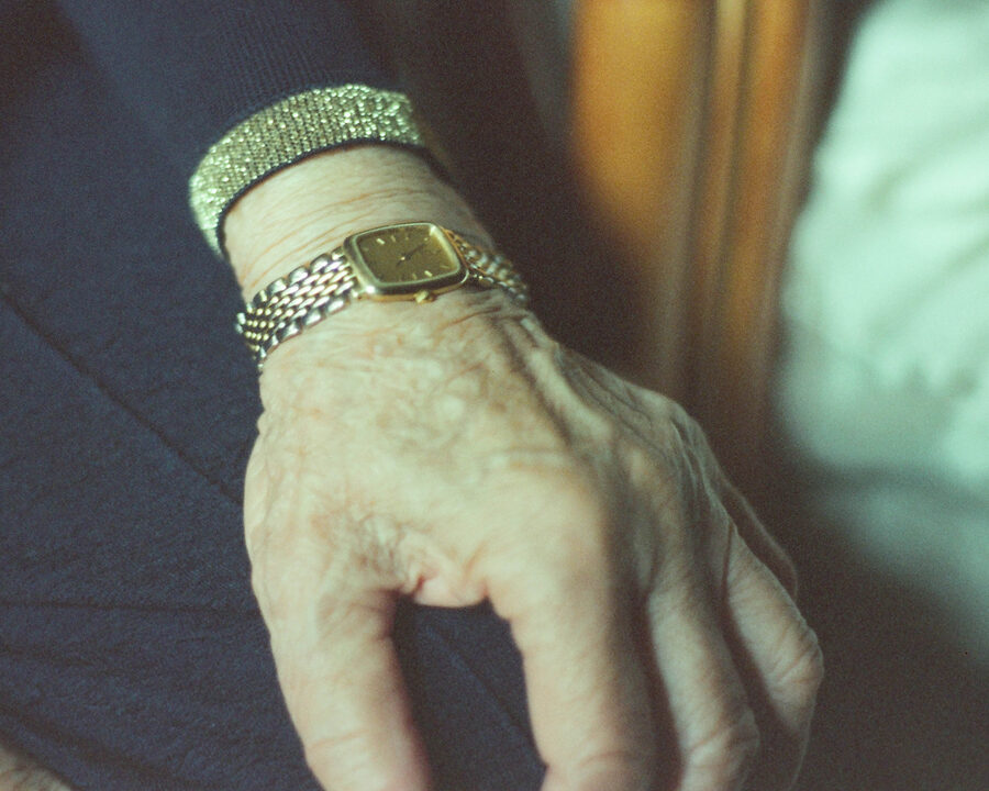 Close-up of an older woman's hand wearing a gold watch and a beaded bracelet